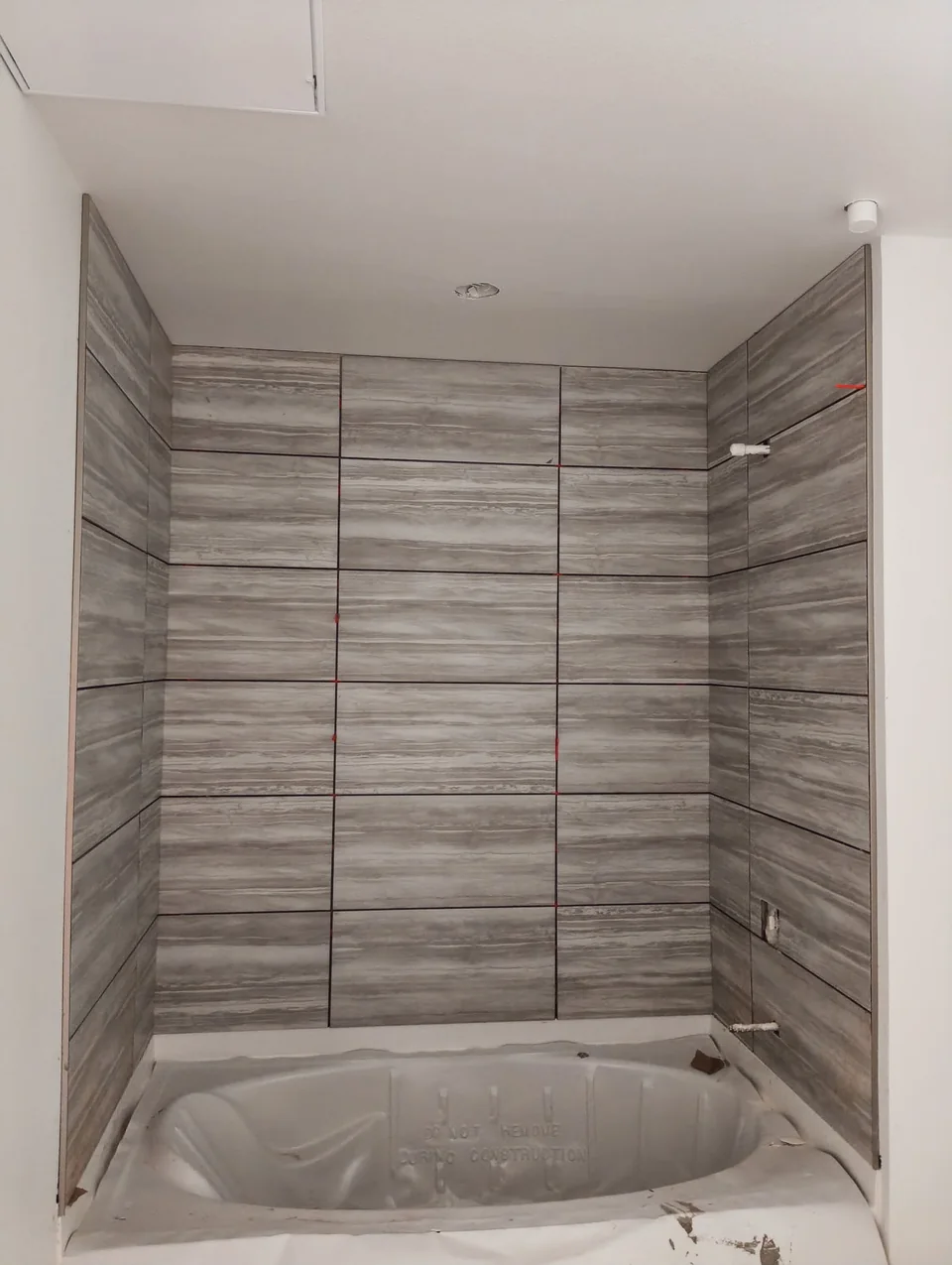 Gray wall tile surrounding a protected bathtub during installation