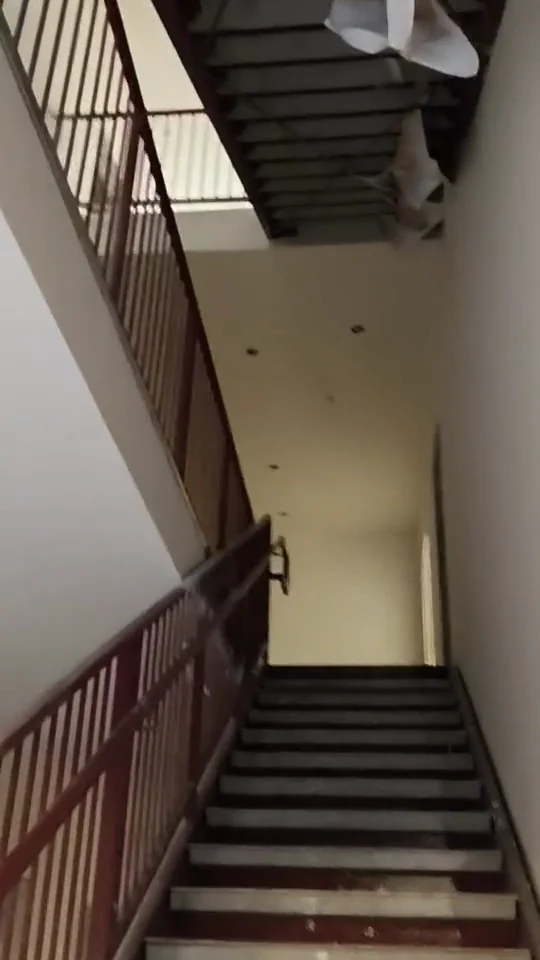 Stairwell with red railings, light walls, and an unfinished ceiling