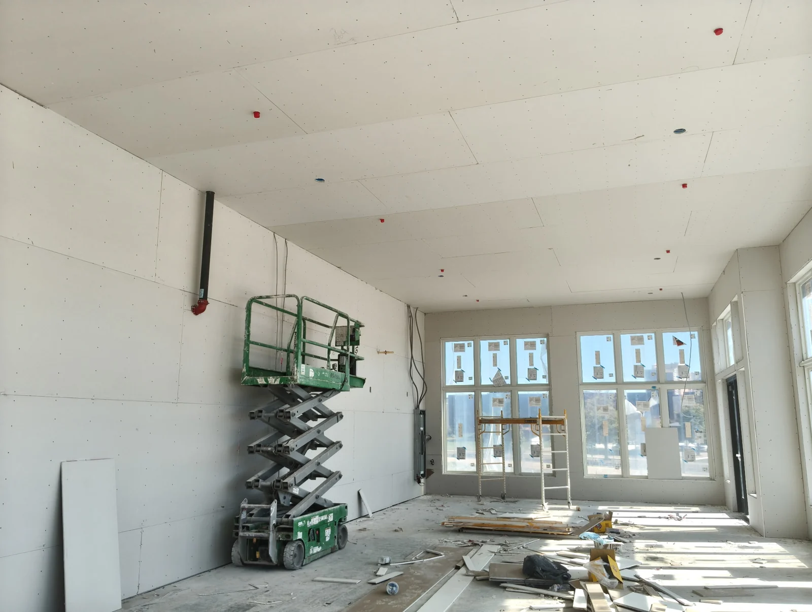 Installed drywall covering the walls and ceiling of a sunlit interior